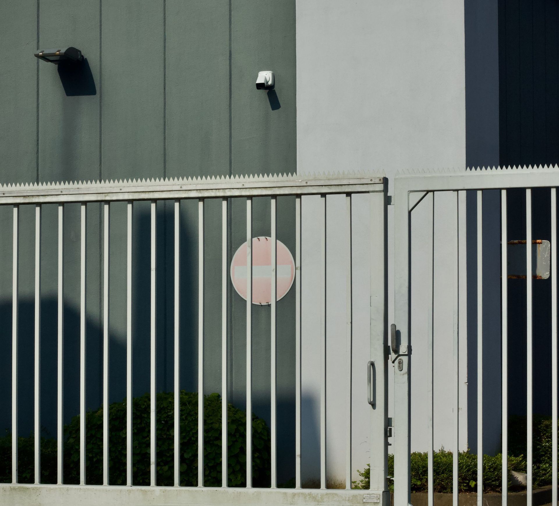 Photo of a secured industrial building with a white metal gate, under clear blue sky.